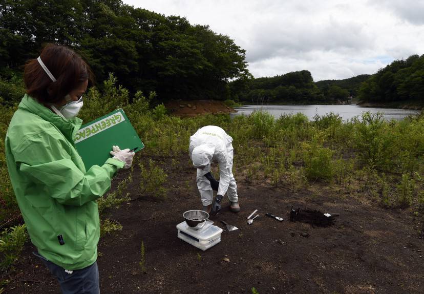 TO GO WITH Japan-nuclear-environment-energy,FOCUS by Natsuko Fukue  This photo taken on July 17, 2015 shows Greenpeace researcher Kazue Suzuki (L) logging information as colleague Jan Vande Putte (R) collects earth samples at the Ganbe Dam lakeside in the village of Iitate in Fukushima prefecture.  Iitate is significant because Japan's government did not order its evacuation until more than a month after the Fukushima nuclear accident began, but post-facto modelling of the radiation plume showed Iitate was right in its path.     AFP PHOTO / TOSHIFUMI KITAMURA        (Photo credit should read TOSHIFUMI KITAMURA/AFP/Getty Images)