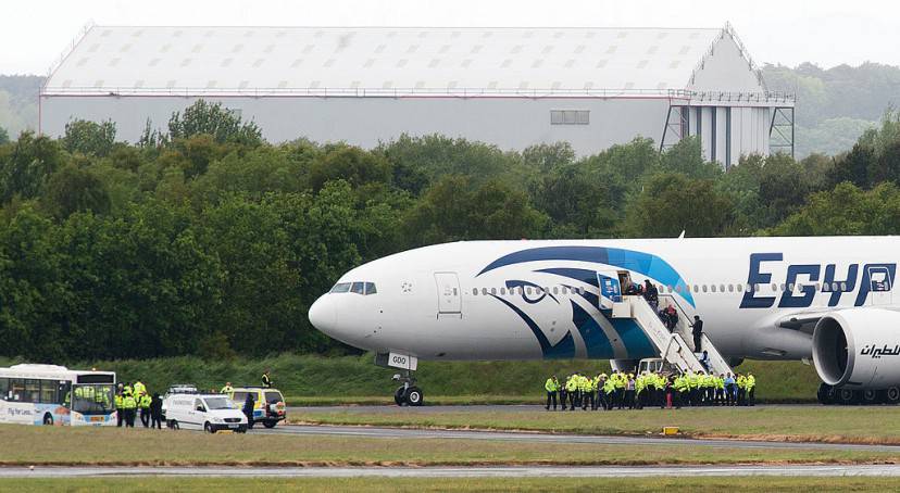 Police escort passengers off the Egyptair Boeing 777 flight from Cairo that was forced to land at Glasgow Prestwick airport in Scotland on June 15, 2013 en route to JFK airport in New York after an onboard incident. Britain's Royal Air Force (RAF) on June 15 escorted an Egyptair plane bound for New York to a Scottish airport following an onboard incident, the Ministry of Defence said. The Boeing 777 was travelling between Cairo and New York when a passenger alerted plane crew that she had found a note reading "I'll set this plane on fire" in the toilet. The message was scrawled in pencil on a napkin and was found by BBC New York producer Nada Tawfik. AFP PHOTO / ANDY BUCHANAN (Photo credit should read Andy Buchanan/AFP/Getty Images)