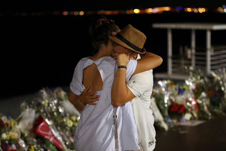 Two people hold each other by the new makeshift memorial on July 18, 2016 in Nice, in tribute to the victims of the deadly Bastille Day attack at the Promenade des Anglais after it was moved from the pavement of the road to the seafront so that the street can be re-opened. France was set to hold a minute's silence on July 18, 2016 to honour the 84 victims of Mohamed Lahouaiej-Bouhlel, a 31-year-old Tunisian who drove a truck into a crowd watching a fireworks display on Bastille Day, but a period of national mourning was overshadowed by bickering politicians. Church bells will toll across the country, and the country will fall silent at midday, a now grimly familiar ritual after the third major terror attack in 18 months on French soil. / AFP / Valery HACHE (Photo credit should read VALERY HACHE/AFP/Getty Images)