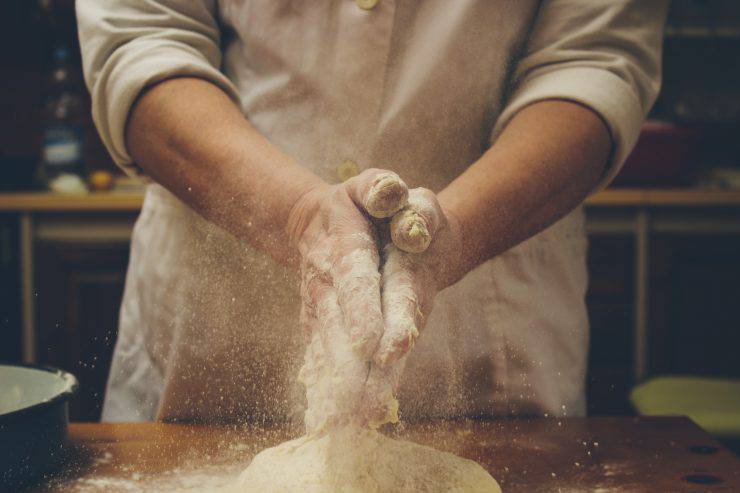 Chef kneading homemade bread, clapping hands full of flour over dough. Retro styled imagery
