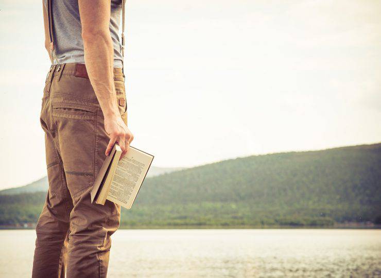 Young Man with book outdoor lake on background Summer vacations and Lifestyle concept