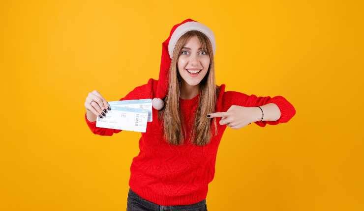 Ragazza con cappello da Babbo Natale indica biglietti aerei