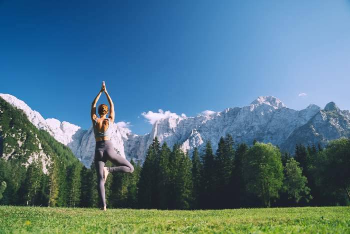 Ragazza nella posizione yoga dell'albero in un prato davanti alle montagne