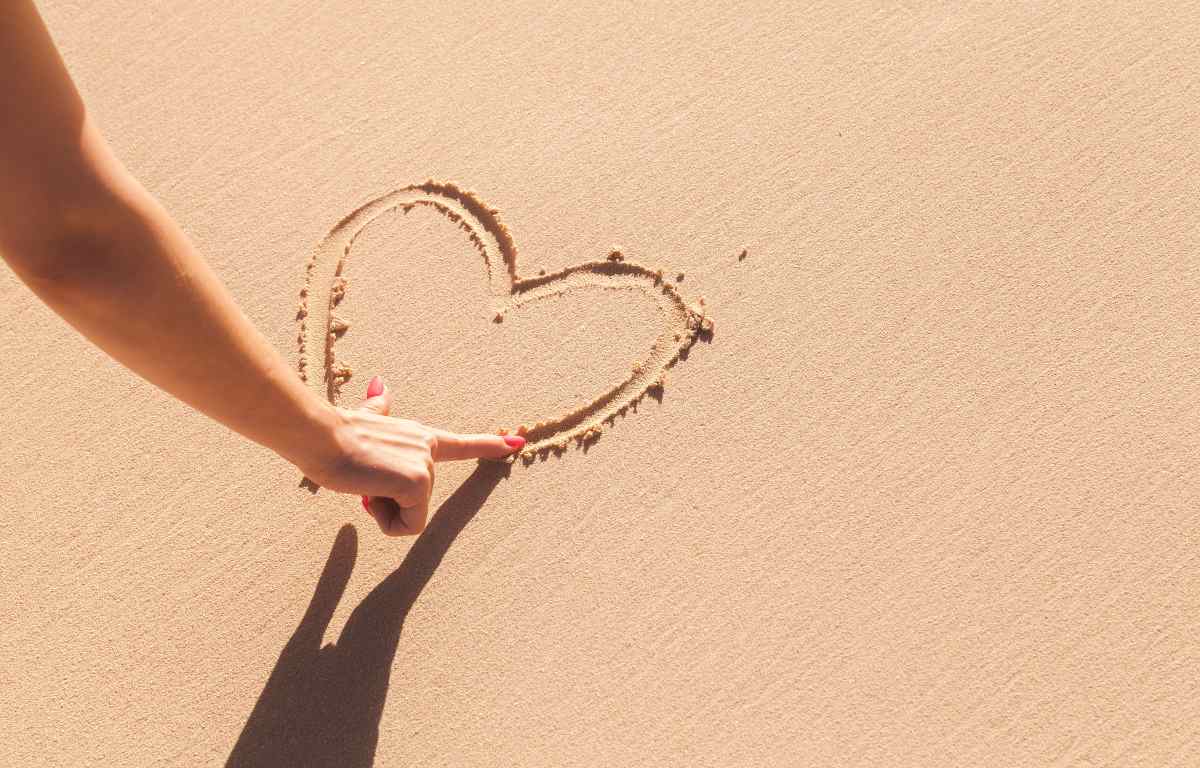 Mando di una donna che disegna un cuore nella sabbia
