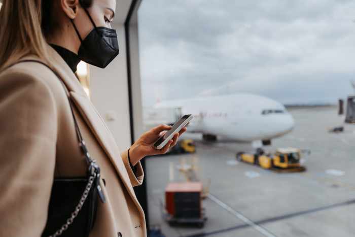 Donna con mascherina controlla il telefono guardando i voli fermi sulla pista