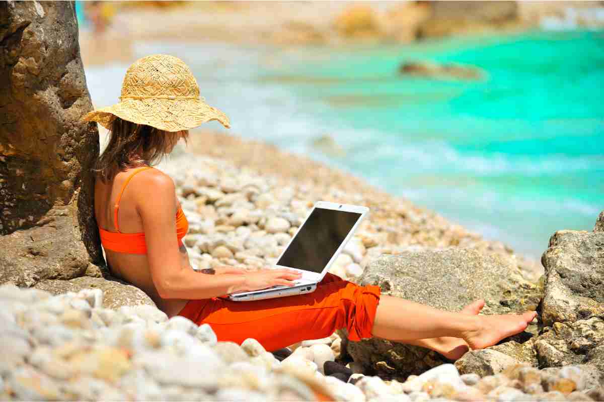 Ragazza che lavora al computer in spiaggia davanti al mare