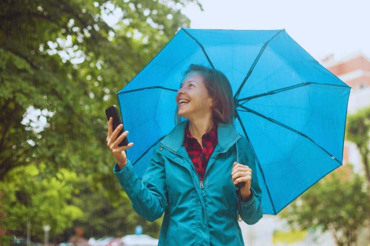 Ragazza sorridente sotto l'ombrello mentre piove