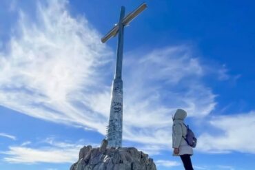 Cielo azzurro ragazza guarda croce bloccata nei massi