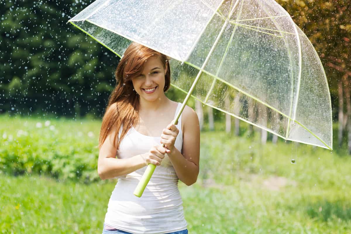 Ragazza che sorride tenendo un ombrello mentre piove