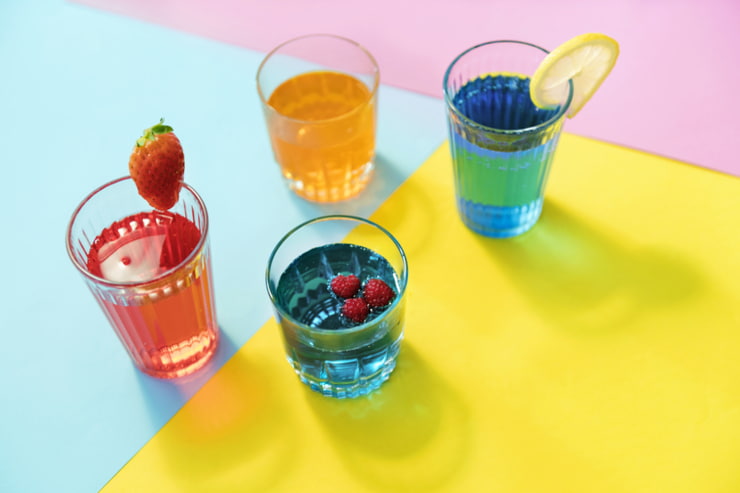 Quattro drink di colori diversi appoggiati su sfondo colorato