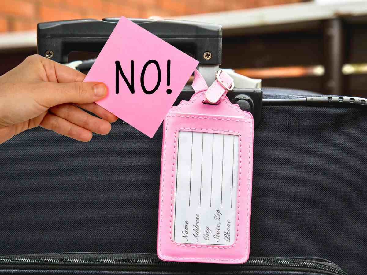 valigia con targhetta e mano con post-it con scritto NO
