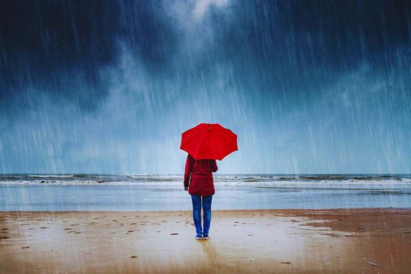 Donna con ombrello che osserva il mare mentre piove