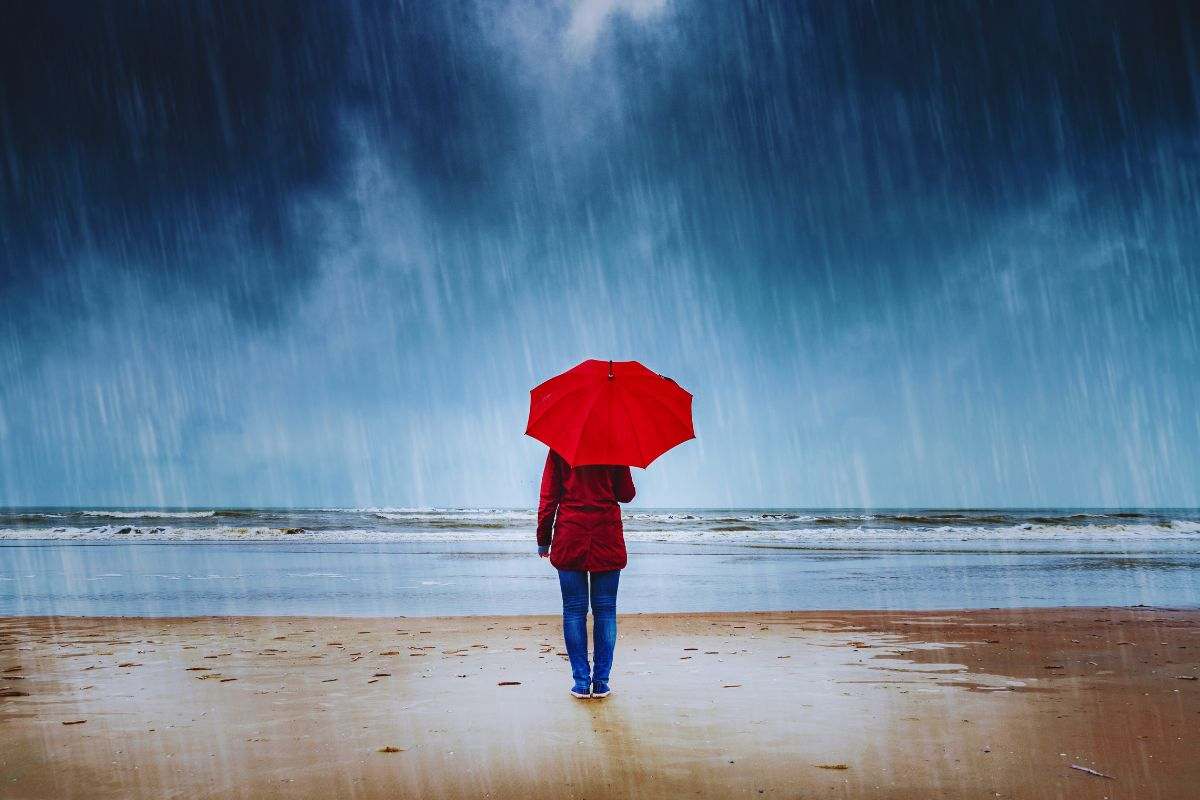 Donna con ombrello che osserva il mare mentre piove