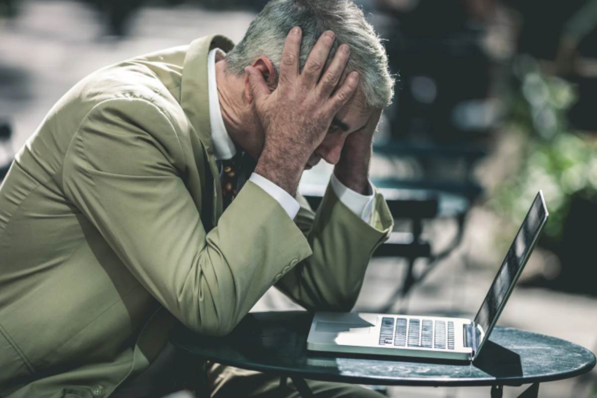 uomo seduto davanti al computer con la testa tra le mani