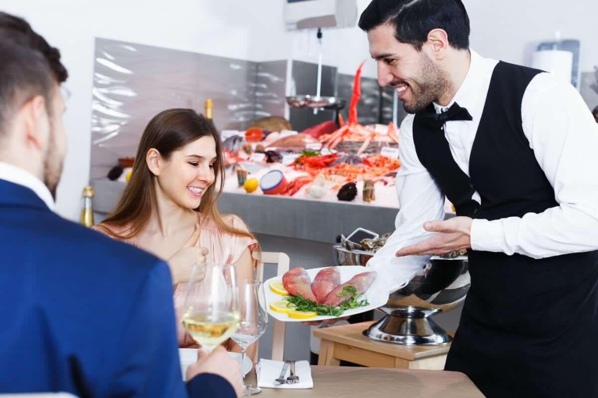 Cameriere serve piatto con del pesce a clienti seduti al tavolo