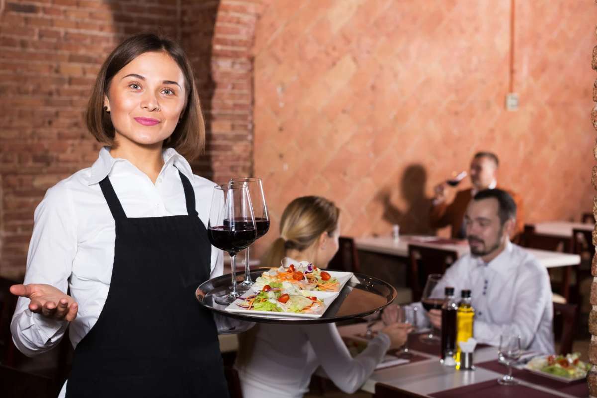 Cameriera con piatto in mano e coppia che mangia