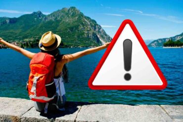 Persona con zaino addosso vicino lago e simbolo pericolo