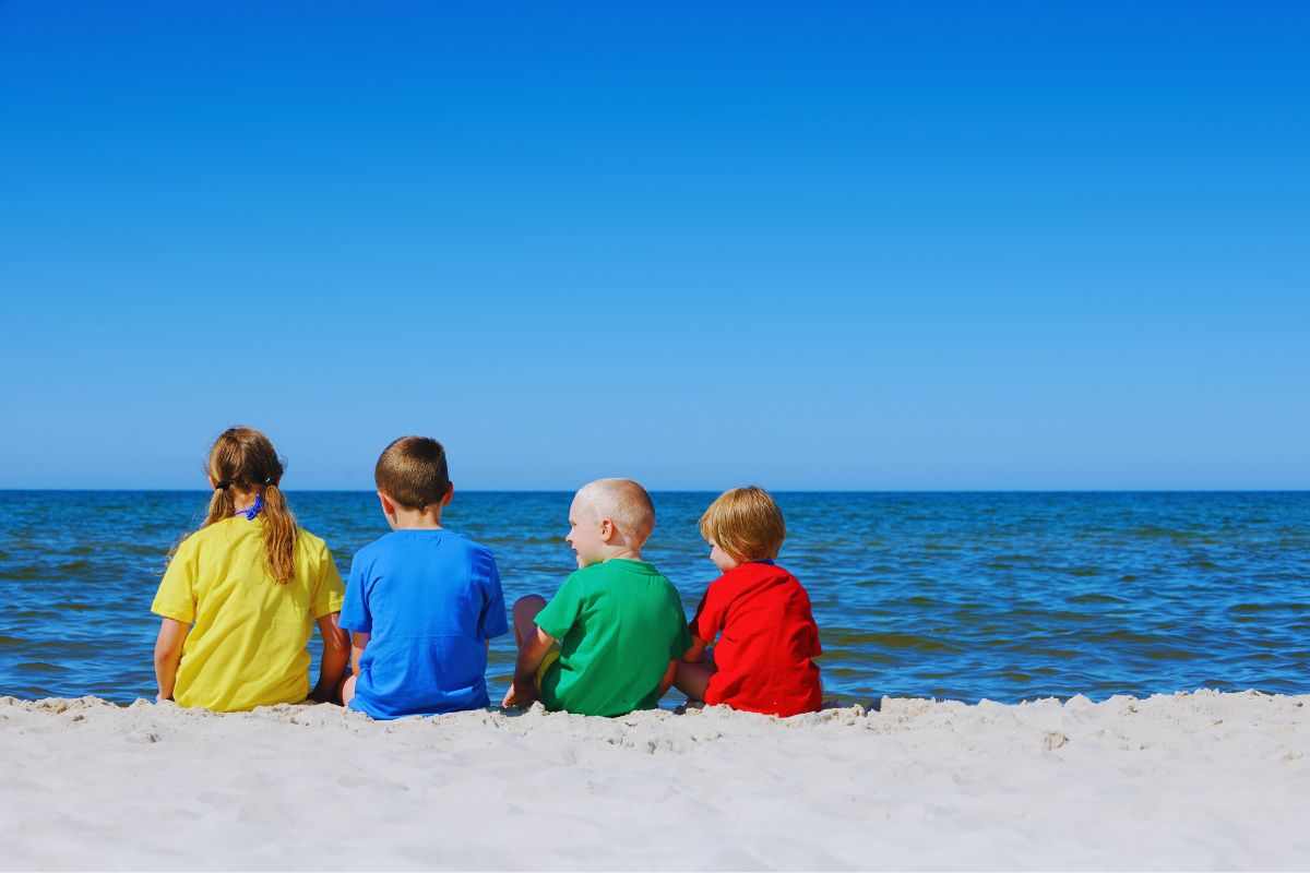 Bimbi seduti in spiaggia che guardano il mare