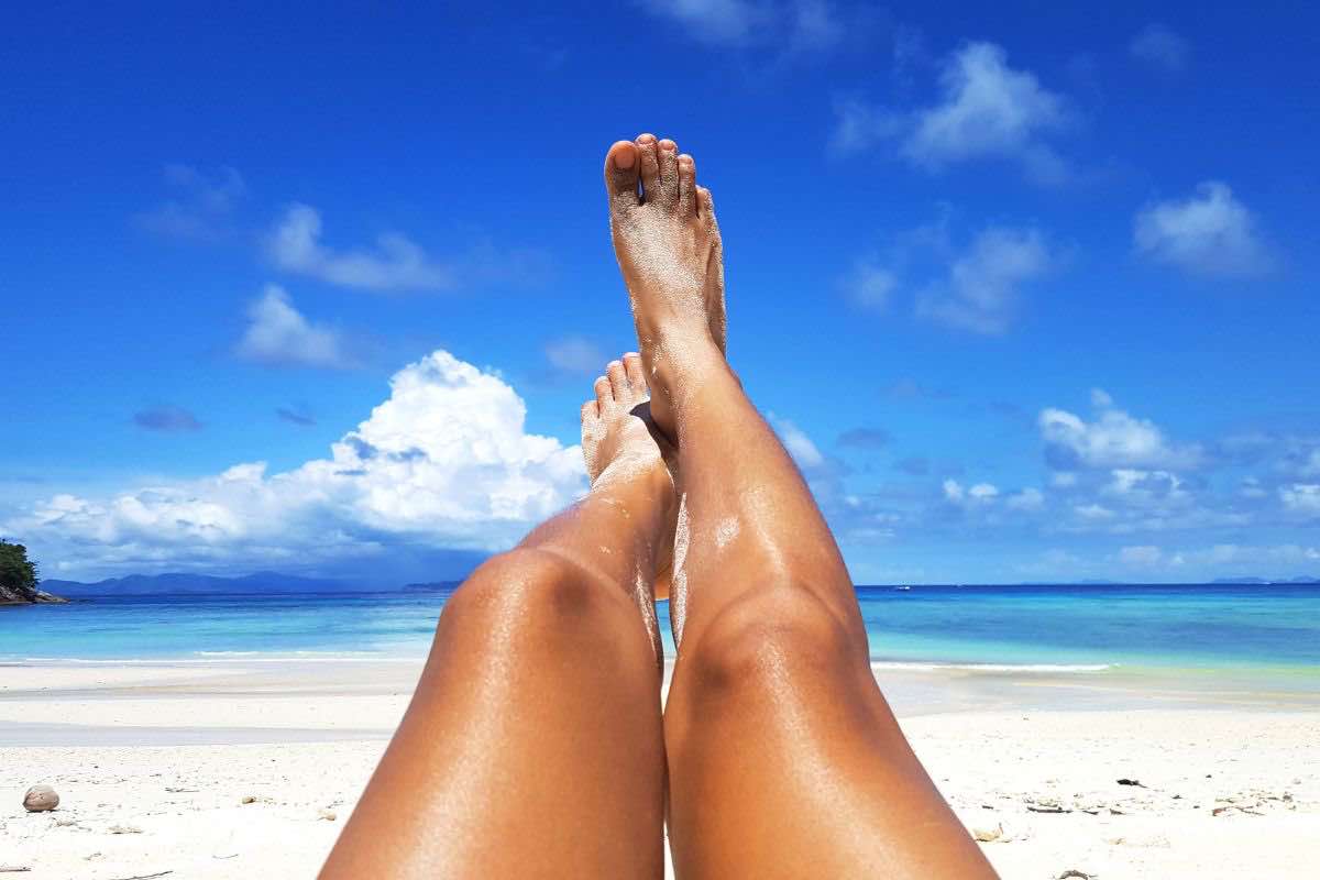 Donna con gambe stese al sole in spiaggia