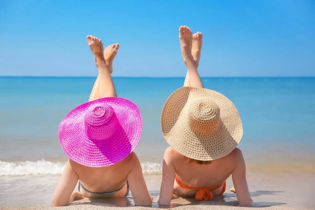 Due donne con cappelli sdraiate sulla riva del mare