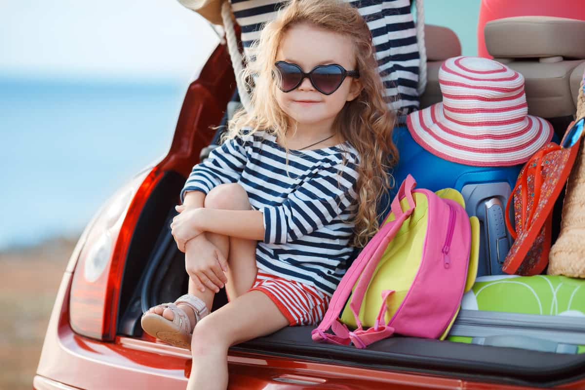 Bambina seduta nel bagagliaio di una macchina piena di valigie
