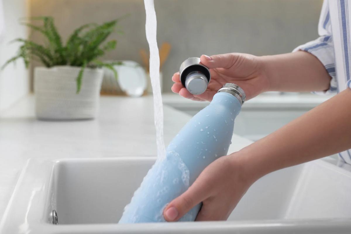 Donna che lava borraccia termica sotto acqua corrente