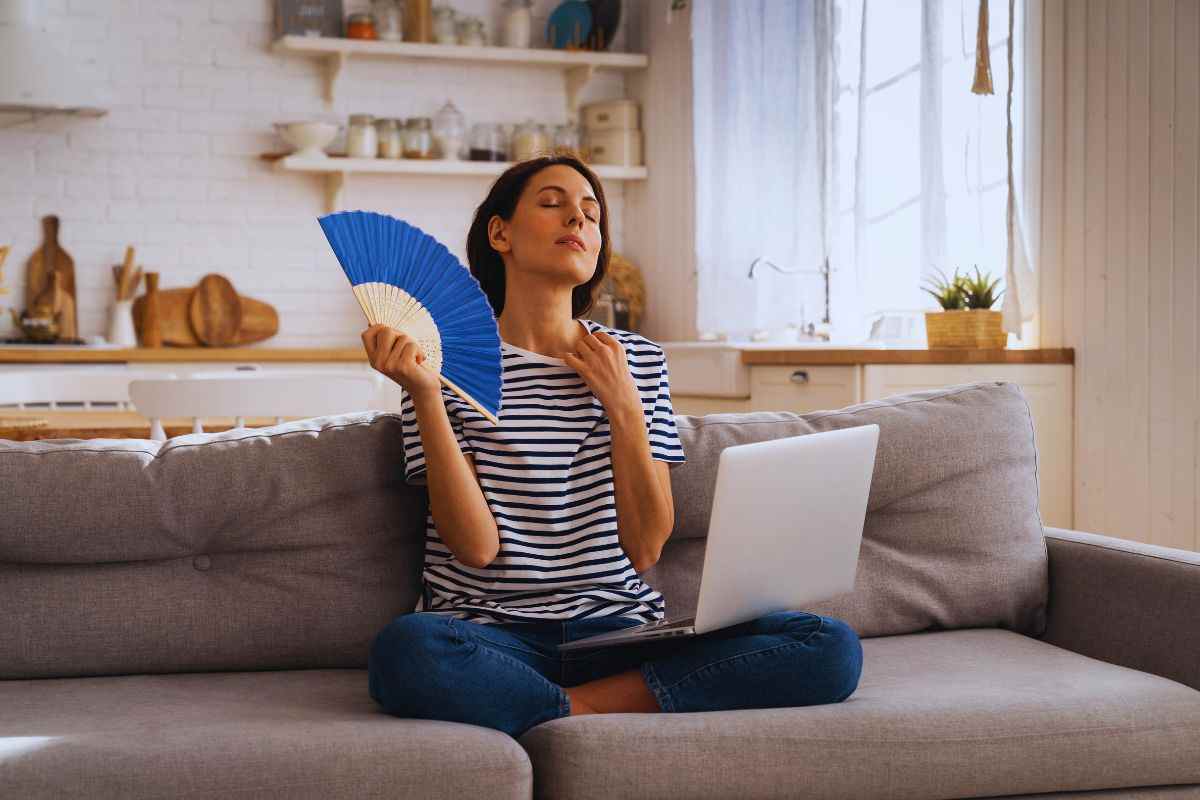 Donna su divano che usa ventaglio per trovare sollievo dal caldo