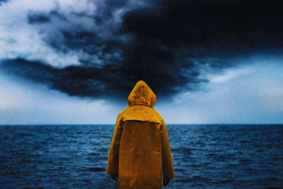 Persona con impermeabile di spalle osserva l'arrivo di una tempesta