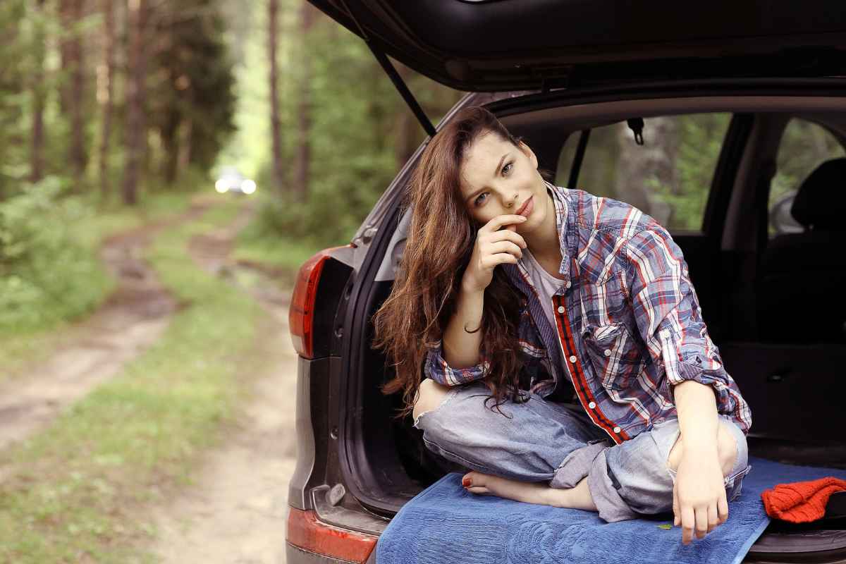 Ragazza seduta sul bagagliaio di un'auto