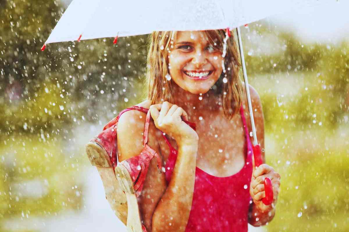 Donna sorridente si protegge da temporale estivo con ombrello
