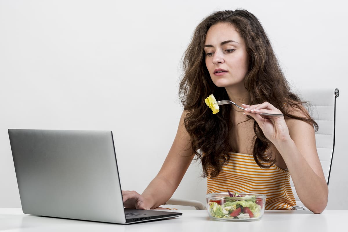Donna preoccupata che mangia e guarda il computer