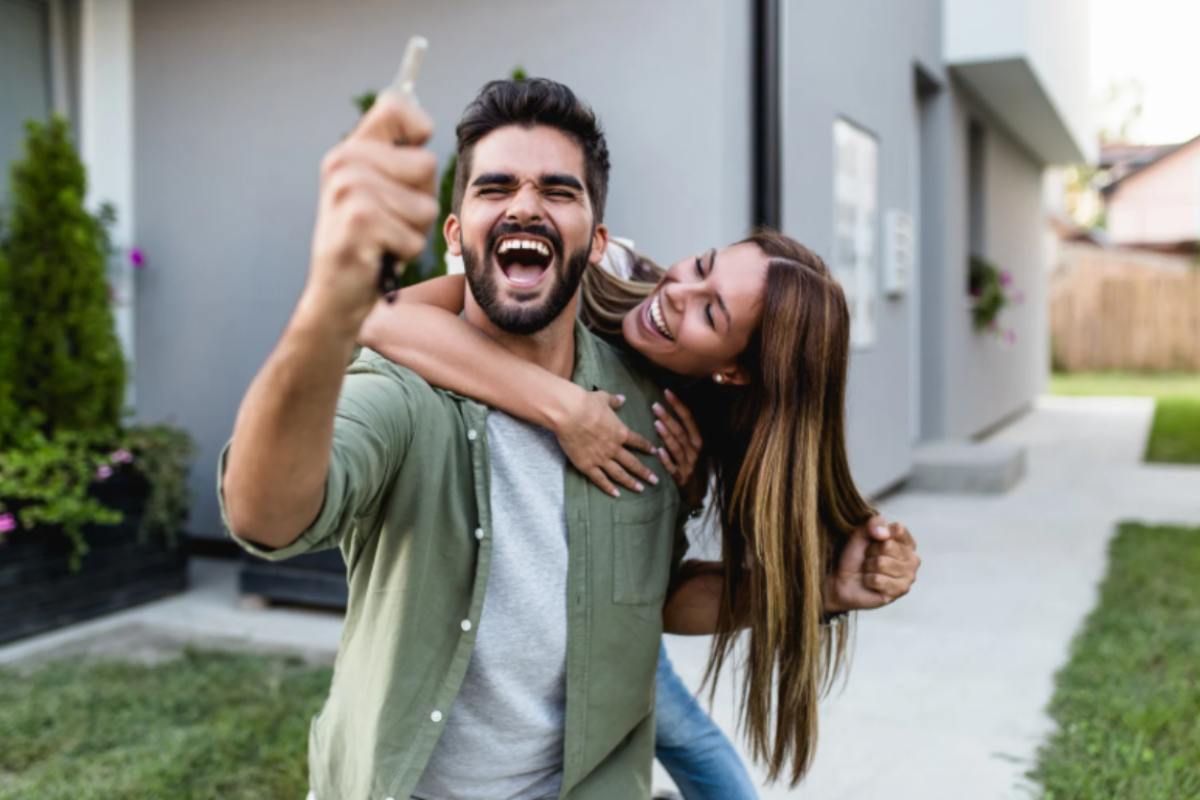 uomo che esulta con una chiave in mano e donna che lo abbraccia da dietro