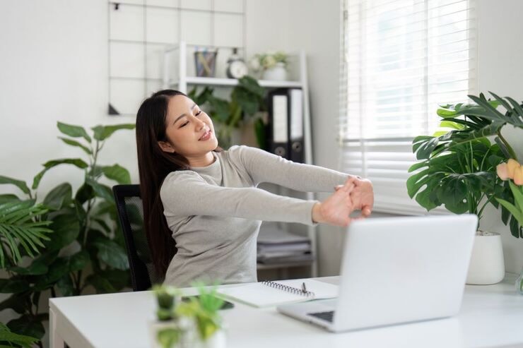 Donna si stiracchia seduta alla scrivania davanti al PC