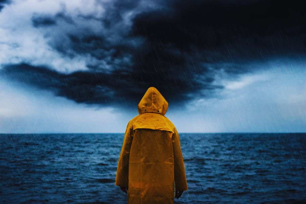 Uomo con impermeabile giallo che osserva mare in tempesta