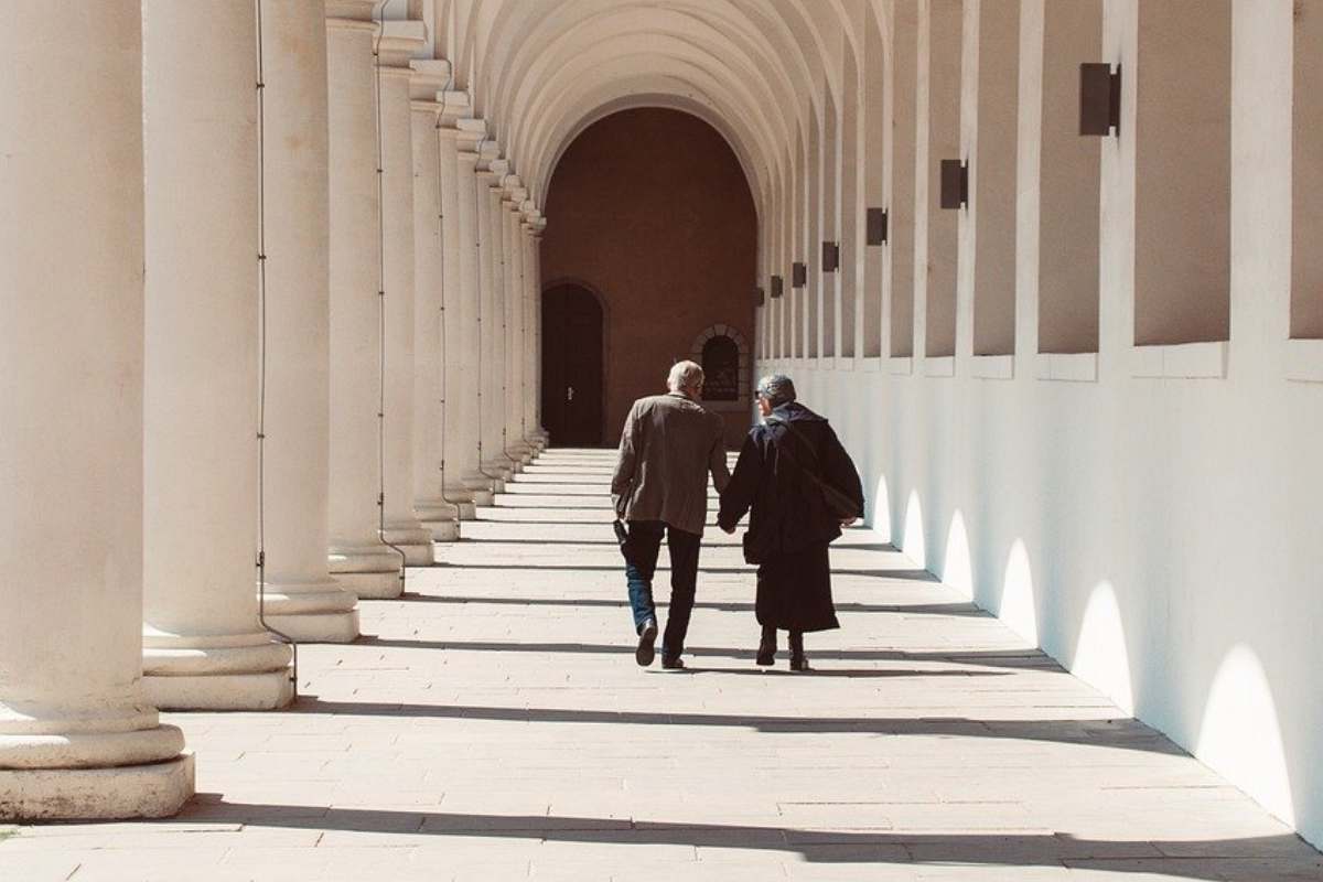 Coppia di anziani che passeggia mano nella mano sotto un portico