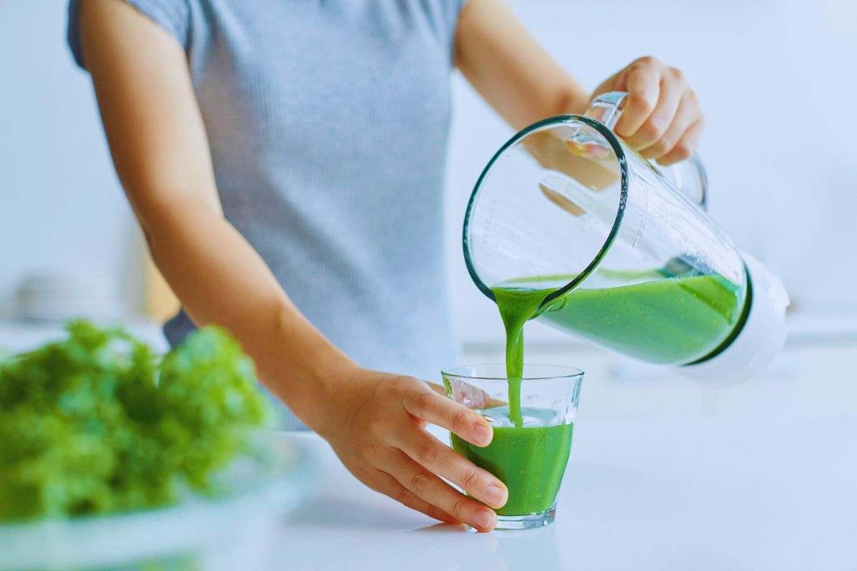 Donna che versa un frullato in un bicchiere di vetro