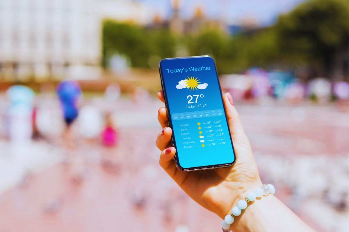 Donna che osserva previsioni meteo su smartphone mentre si trova in spiaggia