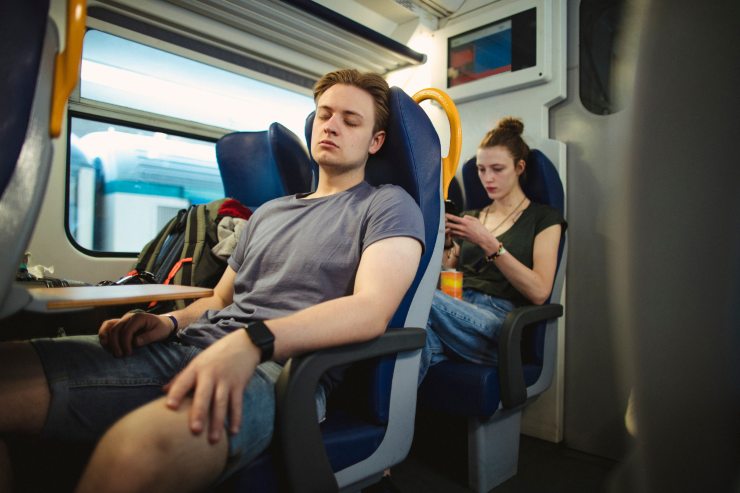ragazzo dorme in treno dietro di lui ragazza al cellulare