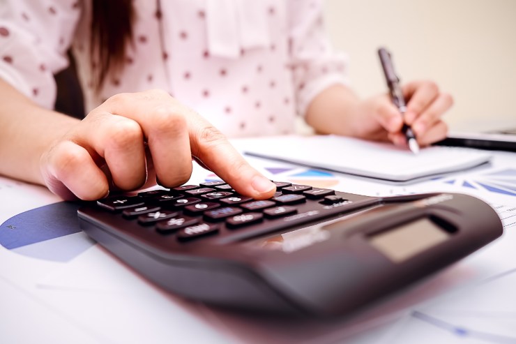 donna fa calcoli con calcolatrici e ha penna in mano e documenti sul tavolo