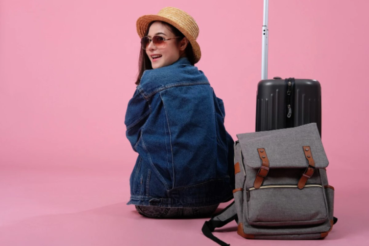 donna seduta con accanto una valigia e uno zaino