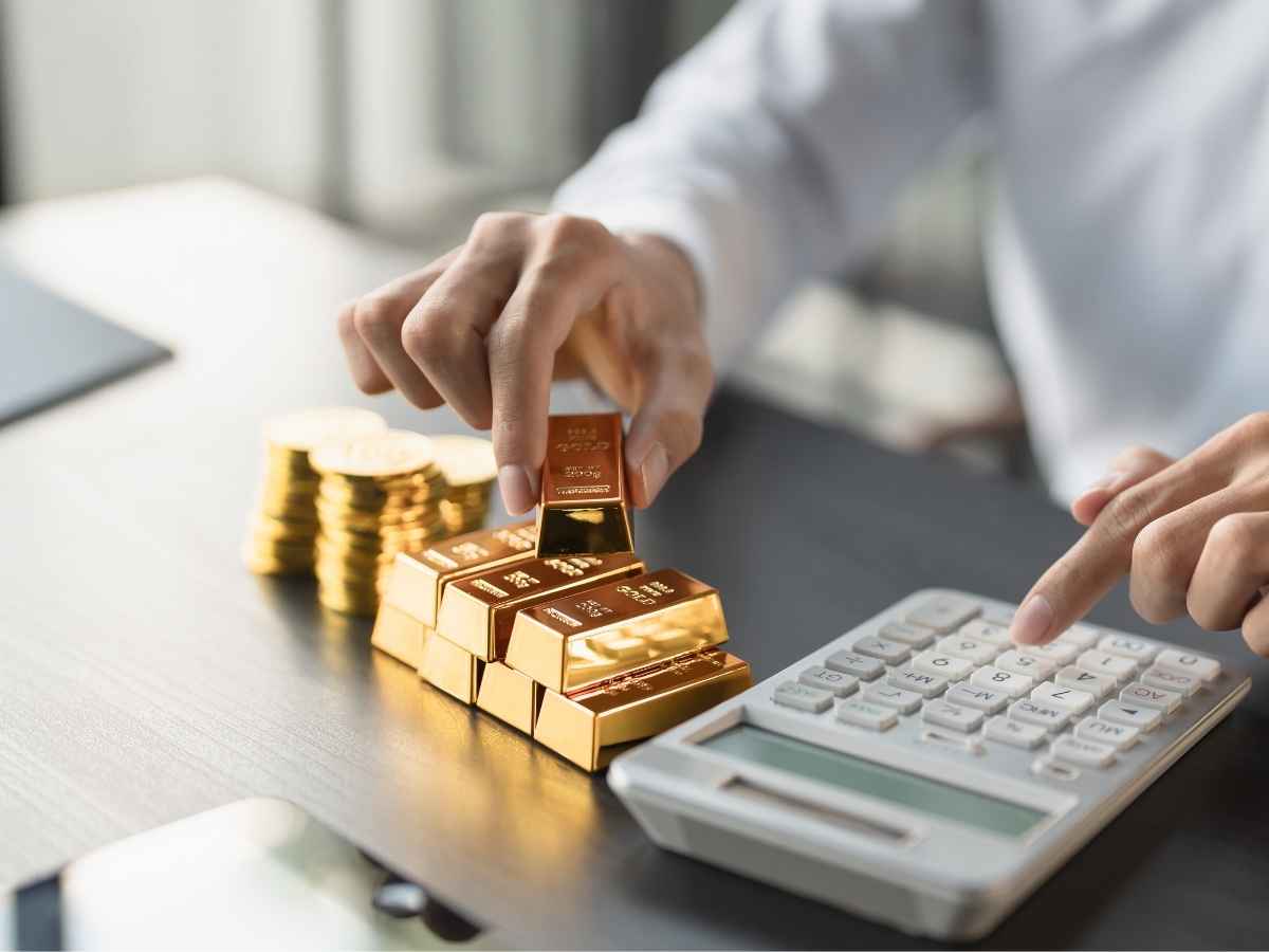Uomo che impila lingotti d'oro e fa calcoli