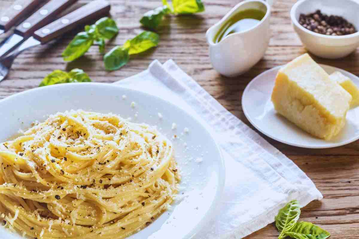 Piatto di cacio e pepe, forma di pecorino, olio d'oliva e pepe poggiati su tavolo