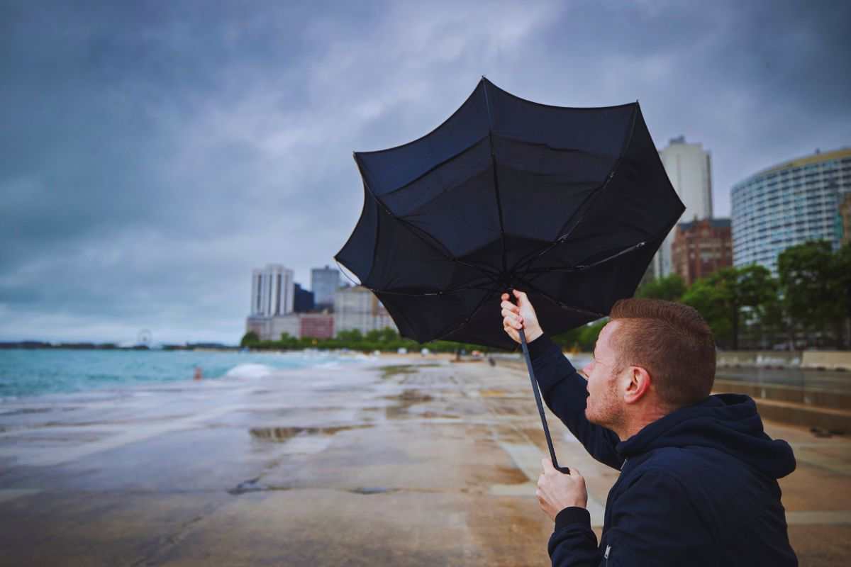 Uomo che cerca di chiudere ombrello trascinato dal vento
