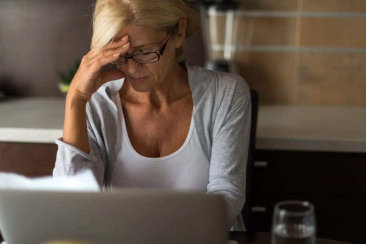 donna anziana davanti al computer preoccupata con una mano sulla fronte