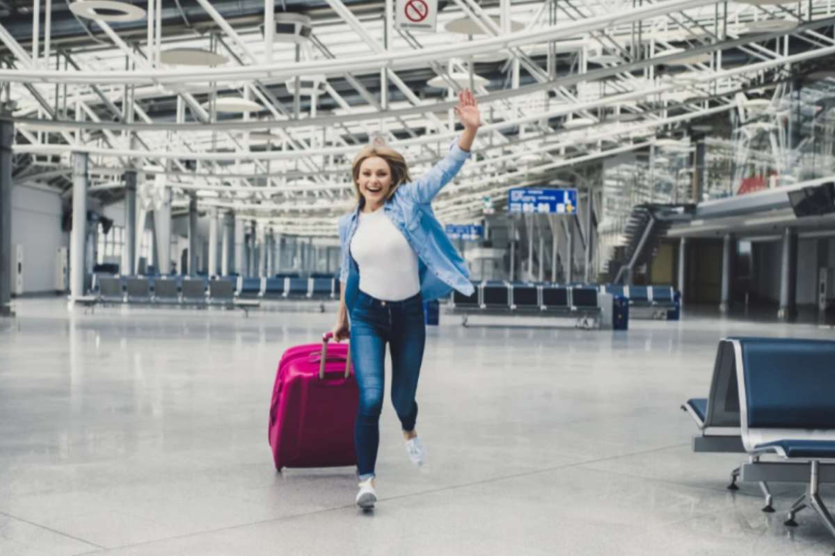 donna felice che corre in aeroporto con un trolley