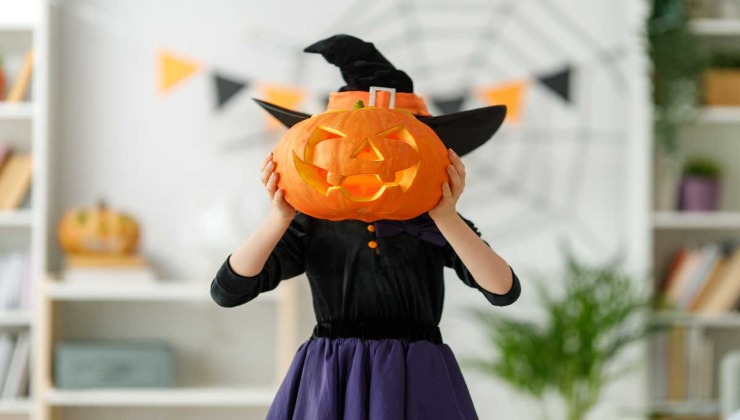 Bimba con costume da halloween che copre il visto con una zucca