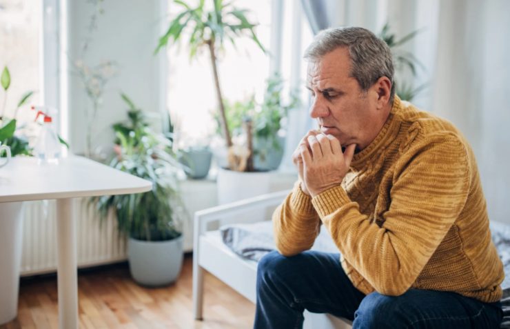 uomo seduto sul divano con le mani sotto al viso e l'espressione preoccupata