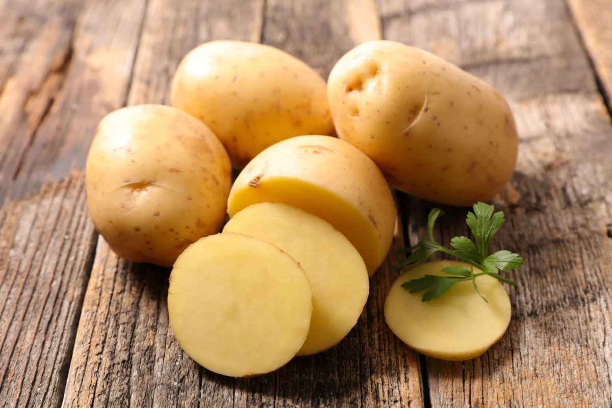Patate crude con buccia e tagliate a fettine su un piano