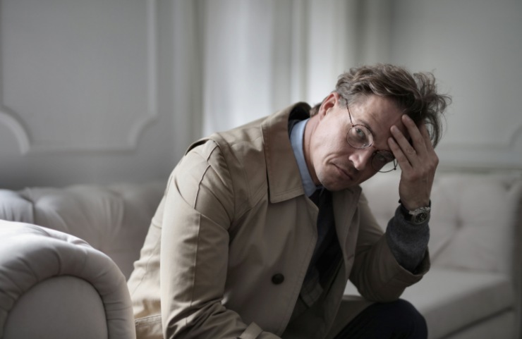 uomo seduto sul divano preoccupato con una mano sulla fronte