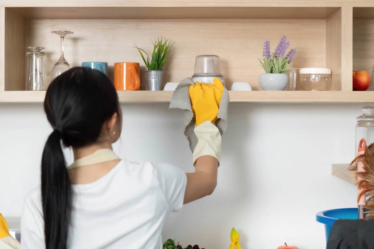 Donna che spolvera mobile con oggetti sopra